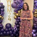 Woman with floral dress stands holding an award.