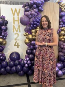 Woman with floral dress stands holding an award.